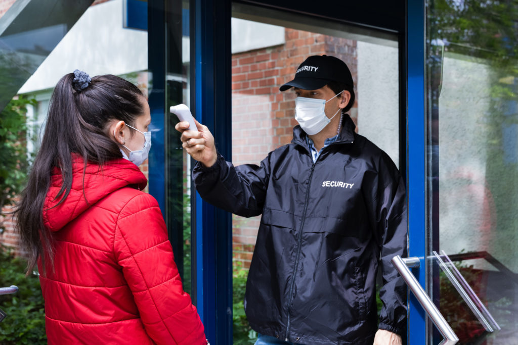 Security Guard Checking Temperature At Building Entrance